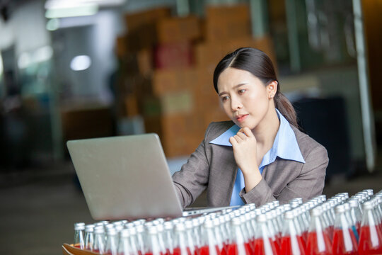 Female Inventory Manager with labtop is checking juice bottles before shipment. Inspection quality control. Manager inspecting production line at drinks production factory