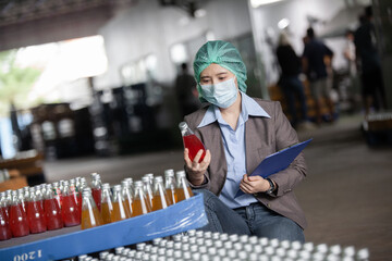 Young female manager factory checking juice bottles before shipment. Inspection quality control. Manager  inspecting production line at drinks production factory