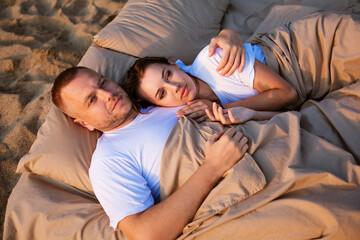 Young couple wrapped in a blanket outdoors. happy couple in love lying and rotating in bed by the sea at sunset. happy caucasian couple of husband and wife wrapped in a blanket outdoors.