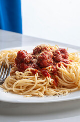 Macro, close up image of a white plate full of spaghetti  with meatballs and toasted garlic salsa on top, lit by a big window on the side vertical 