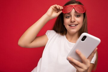 Naklejka premium Photo shot of attractive positive good looking girl wearing casual stylish outfit poising isolated on background with empty space holding in hand and using mobile phone messaging sms looking at