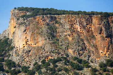 Fototapeta na wymiar View of hundreds of burial tombs carved into mountainside in ancient Lycian city of Pinara in Turkey