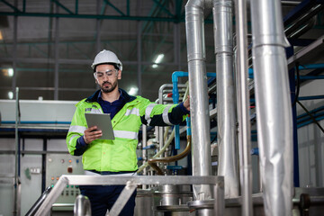 Engineer in uniform holding a tablet in her hands and conducting an inspection at the machine in...