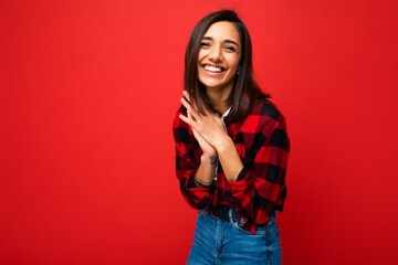 Photo of young beautiful happy smiling brunette woman wearing trendy white t-shirt and red check shirt . Sexy carefree female person posing isolated near red wall in studio with free space. Positive