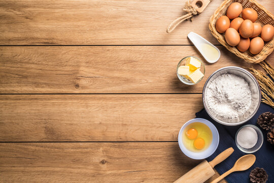 Pictures of ingredients for making cakes bakery around, such as eggs, flour, sugar, butter, recipe book and equipment for making on a wooden floor, with copy space.