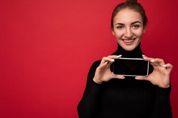 close up Photo of beautiful smiling young woman good looking wearing casual stylish outfit standing isolated on background with copy space holding smartphone showing phone in hand with empty screen