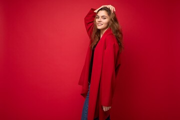 Fototapeta premium Photo of young attractive caucasian hipster woman in trendy casual clothes. Sexy carefree female person posing isolated near red wall in studio. Positive model with natural makeup. Empty space