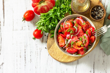 Summer snack or lunch. Fresh tomato salad with onions, herbs and olive oil on a white wooden table. Top view flat lay background. Copy space.