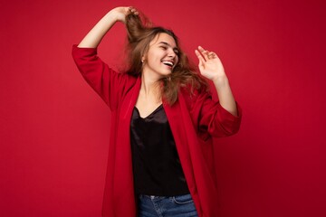 Naklejka premium Photo of young attractive caucasian hipster woman in trendy casual clothes. Sexy carefree female person posing isolated near red wall in studio. Positive model with natural makeup. Empty space