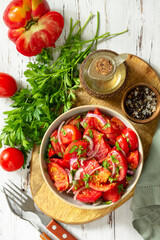 Summer snack or lunch. Fresh tomato salad with onions, herbs and olive oil on a white wooden table. Top view flat lay background.