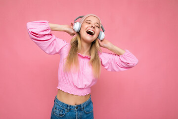 Attractive positive emotional smiling young blonde woman wearing pink blouse and pink hat isolated...