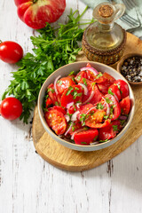 Summer snack or lunch. Fresh tomato salad with onions, herbs and olive oil on a white wooden table. Copy space.