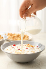 Woman pouring milk from jug into bowl with granola on table
