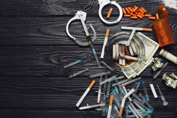 Handcuffs, drugs, money and cigarettes on wooden background. Concept of addiction