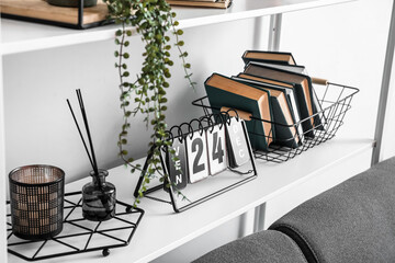 Reed diffuser with books and calendar on shelf near light wall