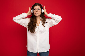 Attractive young brunette female person wearing white shirt and optical glasses isolated over red...
