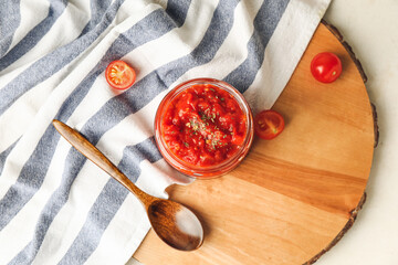Board with glass jar of tasty sauce on light background