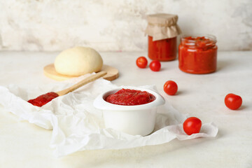 Bowl of tasty sauce and dough on light background