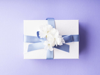 White gift box wrapped with blue ribbon and decor flowers on purple