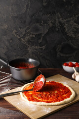 Pizza dough with tasty tomato sauce on dark background