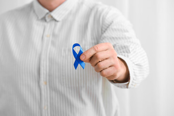 Man with blue ribbon on light background, closeup. Cancer awareness concept
