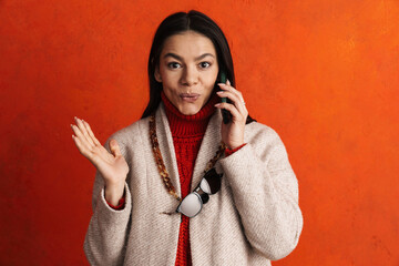 Young hispanic woman expressing surprise while talking on cellphone