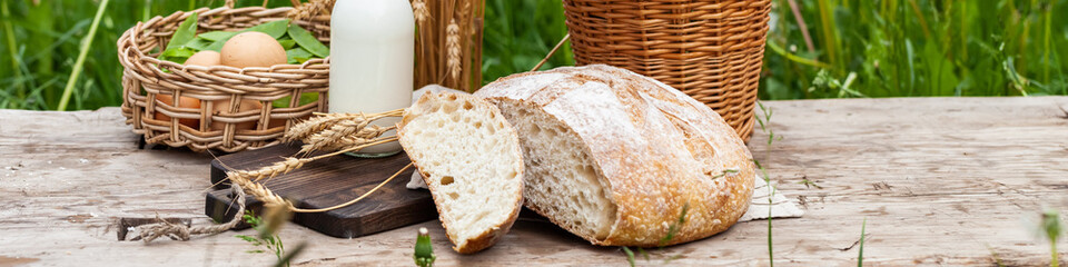 Concept of natural organic products from the local farm. Homemade bread, fresh milk, eggs. Wooden background, outdoors. Close up, copy space for text. Banner