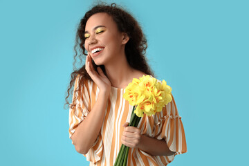 Beautiful young African-American woman with narcissus bouquet on color background