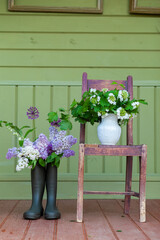 Dark rubber boots with beautiful colorful garden purple lilac flowers. Green fence on background. Countryside style. Copy space for text