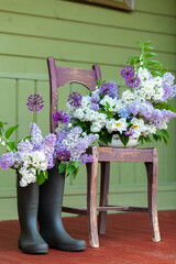Dark rubber boots with beautiful colorful garden purple lilac flowers. Green fence on background. Countryside style. Copy space for text