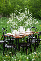 Elegant wedding dinner table decorated with white dishes, flowers in glass vases. Festive atmosphere, luxury party. Sunset, bright summer evening. Close up, details
