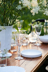 Elegant wedding dinner table decorated with white dishes, flowers in glass vases. Festive atmosphere, luxury party. Sunset, bright summer evening. Close up, details