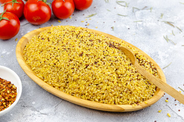 raw bulgur in a bamboo plate on grey table with tomatoes and seasoning