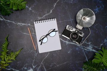 Above view of retro camera and empty notebook on marble background.