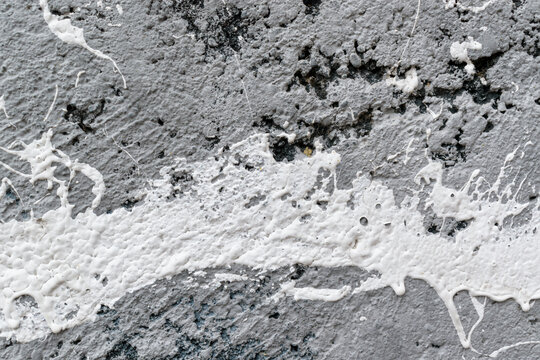 Splash of white paint on a gray concrete wall. Black cavities, depressions.