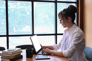Side view of female student sitting in library and using laptop computer.