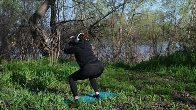  4k video woman doing squat exercise outdoors in headphones