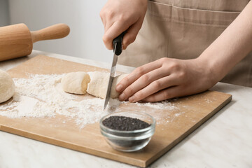 Female chef cutting raw dough on kitchen table, closeup