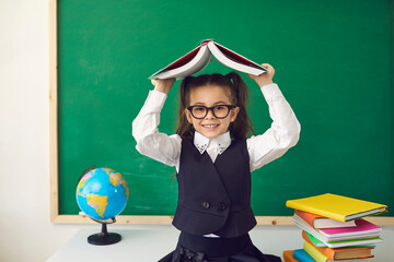 Back to school concept. Little girl with a book over her head smiling is studying in class.