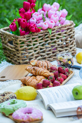 Outdoors picnic in a lush green park with a tasty croissant, fruits, donuts and wine on grass. Summer picnic on the blanket.