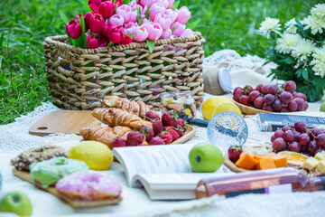 Outdoors picnic in a lush green park with a tasty croissant, fruits, donuts and wine on grass. Summer picnic on the blanket.