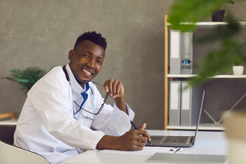 Happy black doctor working on computer. Portrait of young Afro American man in professional medical...