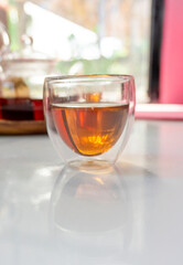 A glass of hot black tea on the white table.