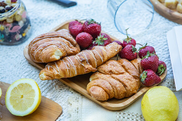 Outdoors picnic in a lush green park with a tasty croissant, fruits, donuts and wine on grass. Summer picnic on the blanket.