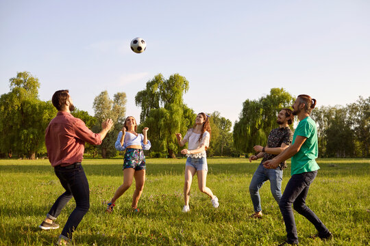 Cheerful friends play with a ball on the grass in a summer park.