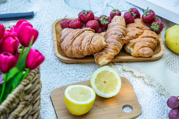 Outdoors picnic in a lush green park with a tasty croissant, fruits, donuts and wine on grass. Summer picnic on the blanket.