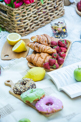 Outdoors picnic in a lush green park with a tasty croissant, fruits, donuts and wine on grass. Summer picnic on the blanket.