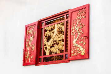 Red ornamented window at Thean Hou Temple, Kuala Lumpur, Malaysia. Chinese temple window decorated with golden motifs of pine, bamboo, and plum. Wooden relief of the Three Friends of Winter.