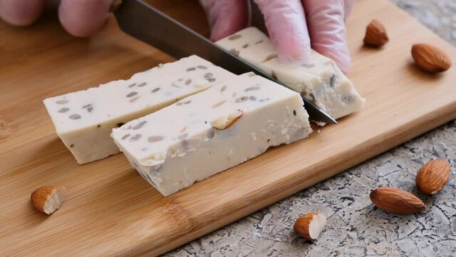 Cut the nut halva with almonds and sunflower seeds into pieces with a knife. Traditional oriental dessert. Close-up.
