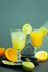 two glasses with a refreshing citrus drink or lemonade or alcoholic cocktail, a pair vintage goblets among sliced lemons, oranges and limes